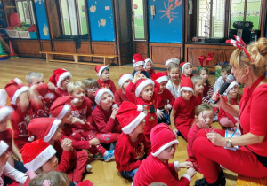 Dzieci przedszkolne podczas zabawy Mikołajkowej uważnie słuchają listu od Świętego Mikołaja czytanego przez nauczycielkę